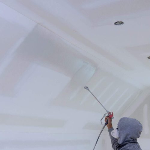 The worker using spray gun with a primer paint walls and ceiling